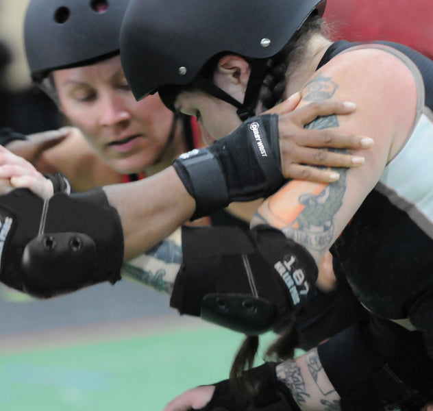 A group of women in 187 Killer Pads roller derby gear huddling on a track.