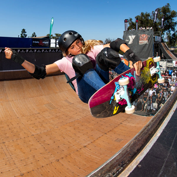 Skateboarder performing a trick on a half-pipe with a crowd watching wearing 187 Killer Pads.